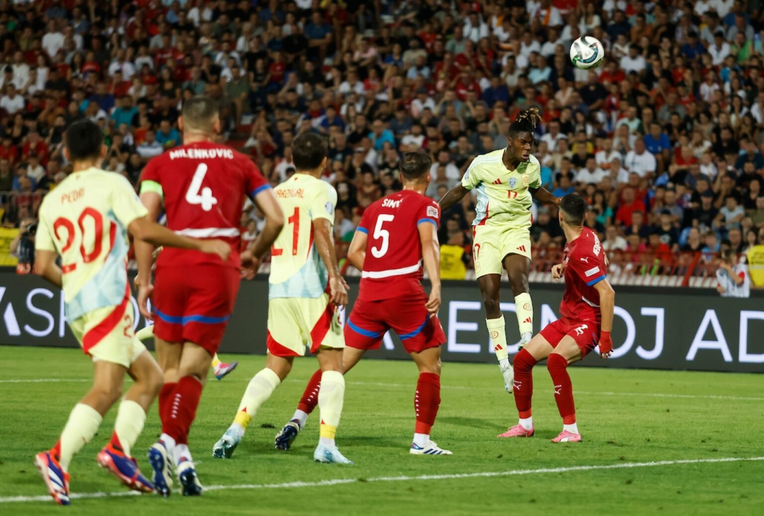 Игрок сборной Испании выигрывает верховую борьбу в матче против Сербии на заполненном стадионе