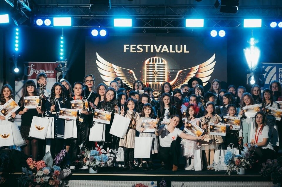Участники и победители IX фестиваля «Voci de Îngeri» на сцене в Сучаве на фоне логотипа фестиваля с золотым микрофоном и крыльями