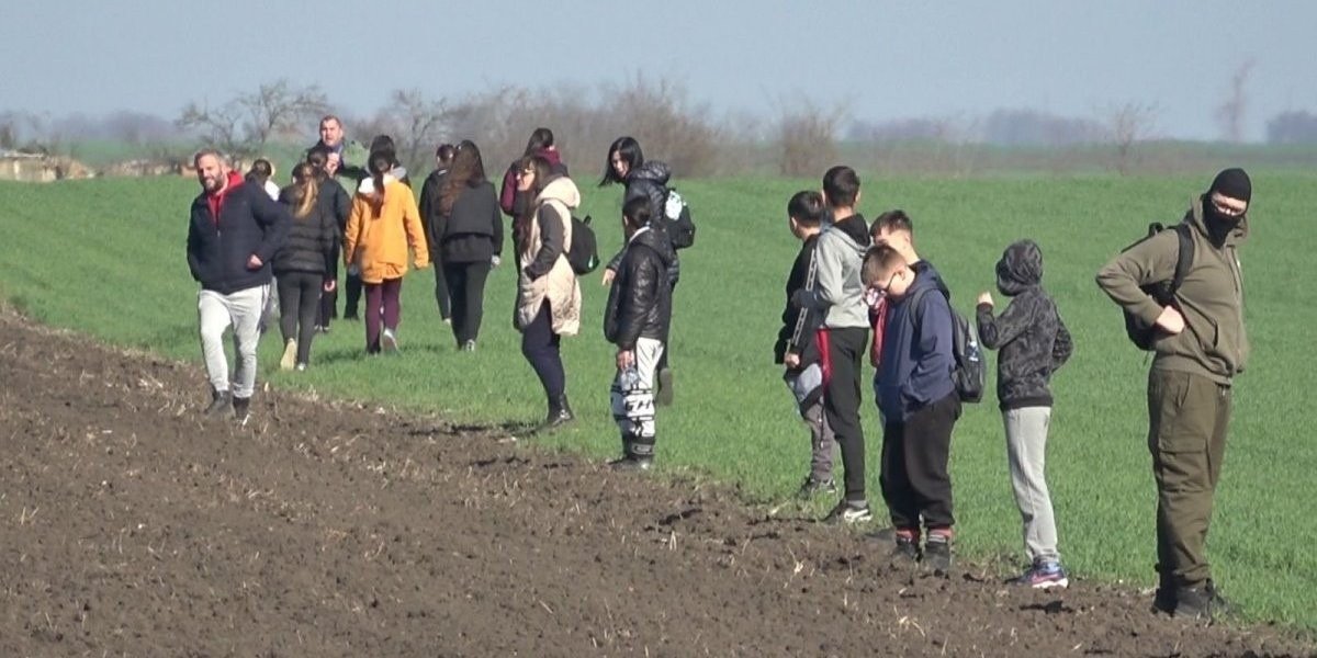 Группа школьников на краю зелёного поля общается с егерем во время подсчёта зайцев