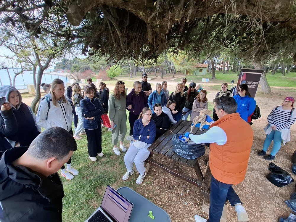 Группа студентов собралась вокруг стола на открытом воздухе для анализа собранного морского мусора на побережье Пулы