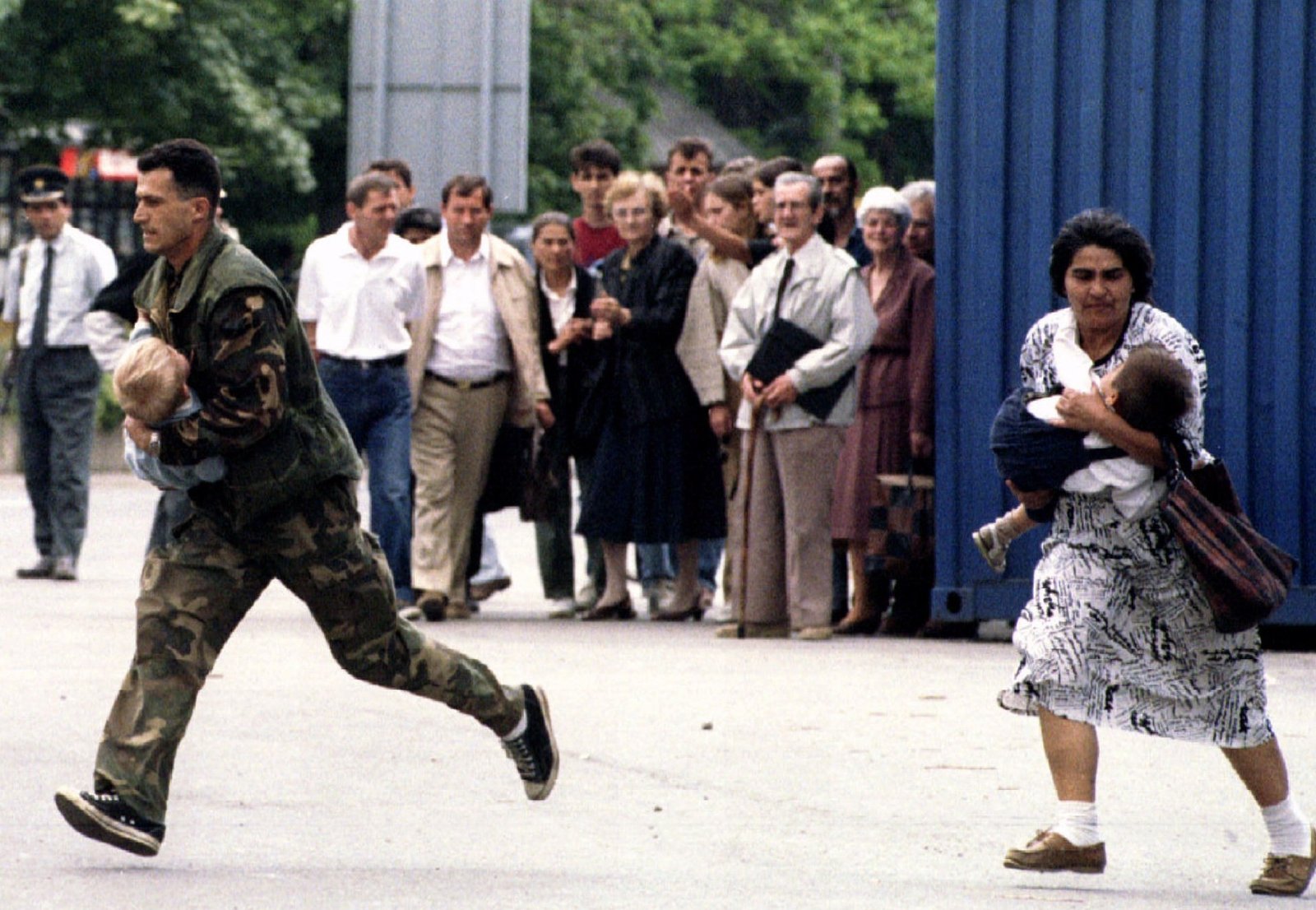 Осада Сараево, 1995 год. Солдат и женщина бегут с детьми на руках на фоне толпы жителей, пытающихся укрыться от обстрела