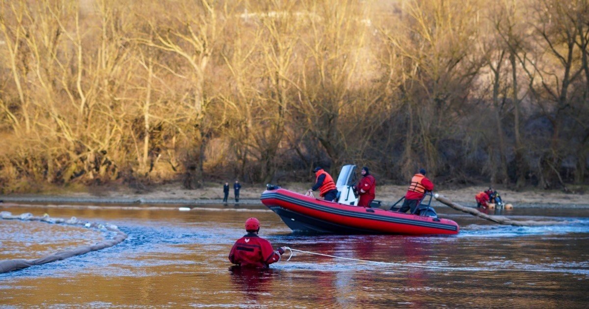 Спасательная операция на загрязнённом Днестре — спасатель в воде координирует работу с моторной лодкой на фоне потемневшей от нефтепродуктов реки