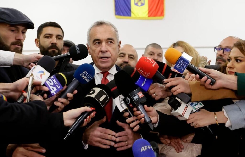 Кэлин Джорджеску даёт пресс-конференцию в окружении микрофонов румынских и международных СМИ на фоне флага Румынии