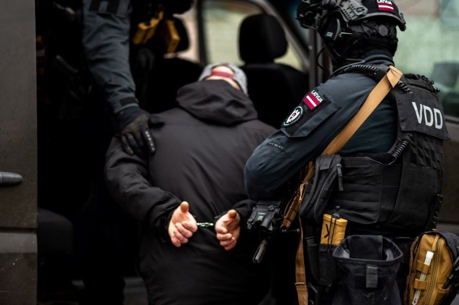 Сотрудники Службы государственной безопасности Латвии (VDD) конвоируют задержанного в наручниках