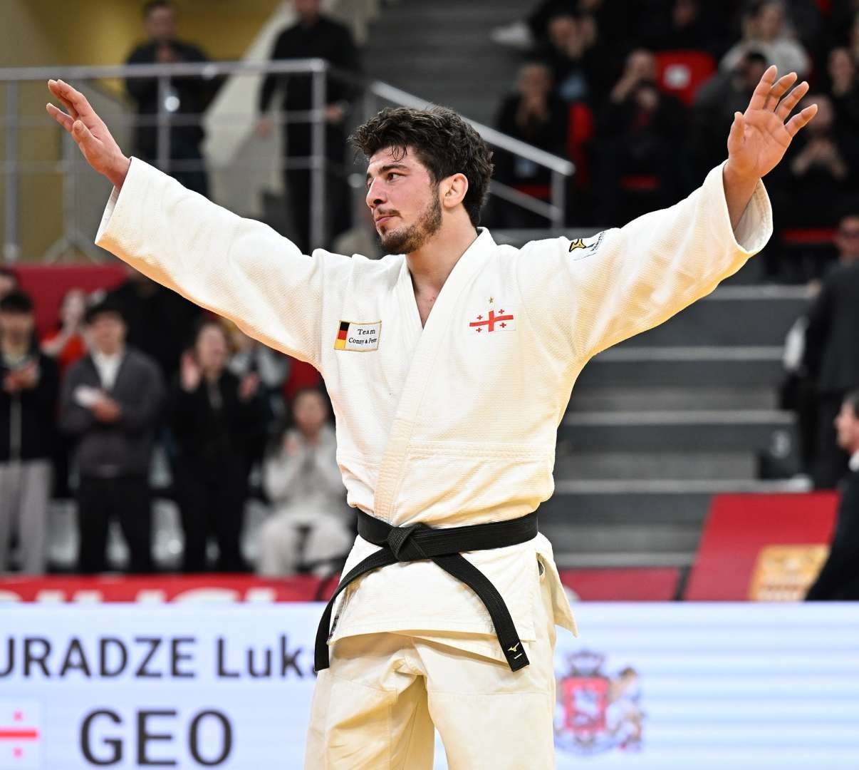 Грузинский дзюдоист Лука Майсурадзе с поднятыми руками празднует победу на Tbilisi Grand Slam перед аплодирующими зрителями