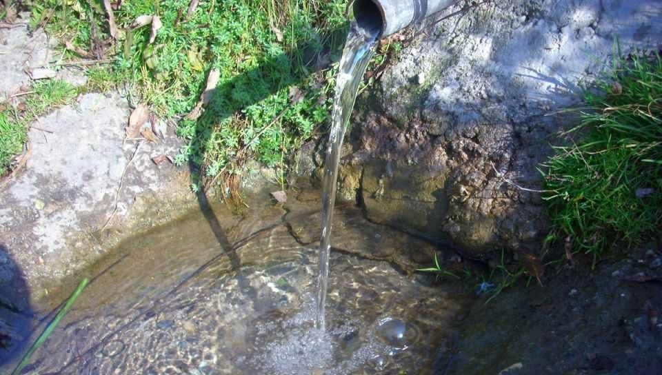 Вода течёт из трубы в каменный бассейн природного источника в сельской местности жудеца Алба