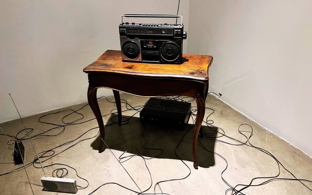 Старинный радиоприёмник на антикварном деревянном столике с разбросанными кабелями и проводами в галерейном пространстве