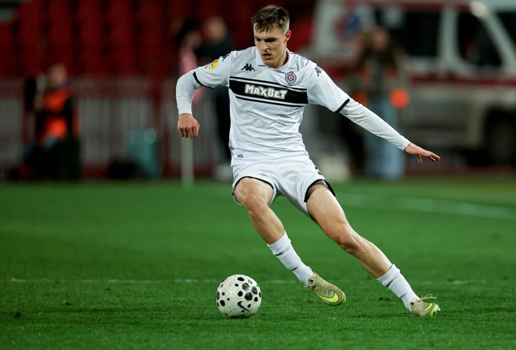 Андрей Костич ведёт мяч в матче за «Партизан» в белой гостевой форме клуба