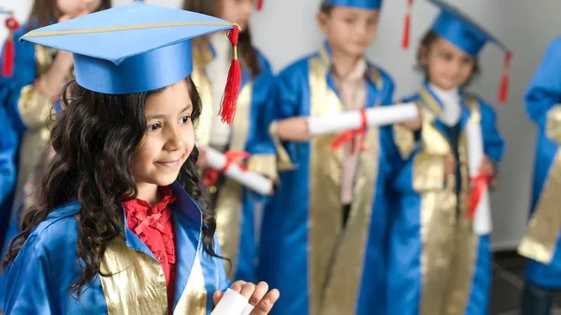 Дети в синих выпускных мантиях и шапочках с дипломами на школьной церемонии окончания четвёртого класса