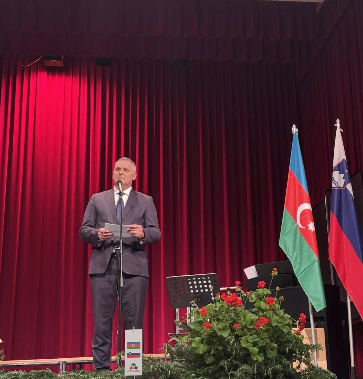Словенский министр Боян Кумер выступает на памятной церемонии в честь Мехти Гусейнзаде в Шемпасе (Словения) на фоне флагов Азербайджана и Словении