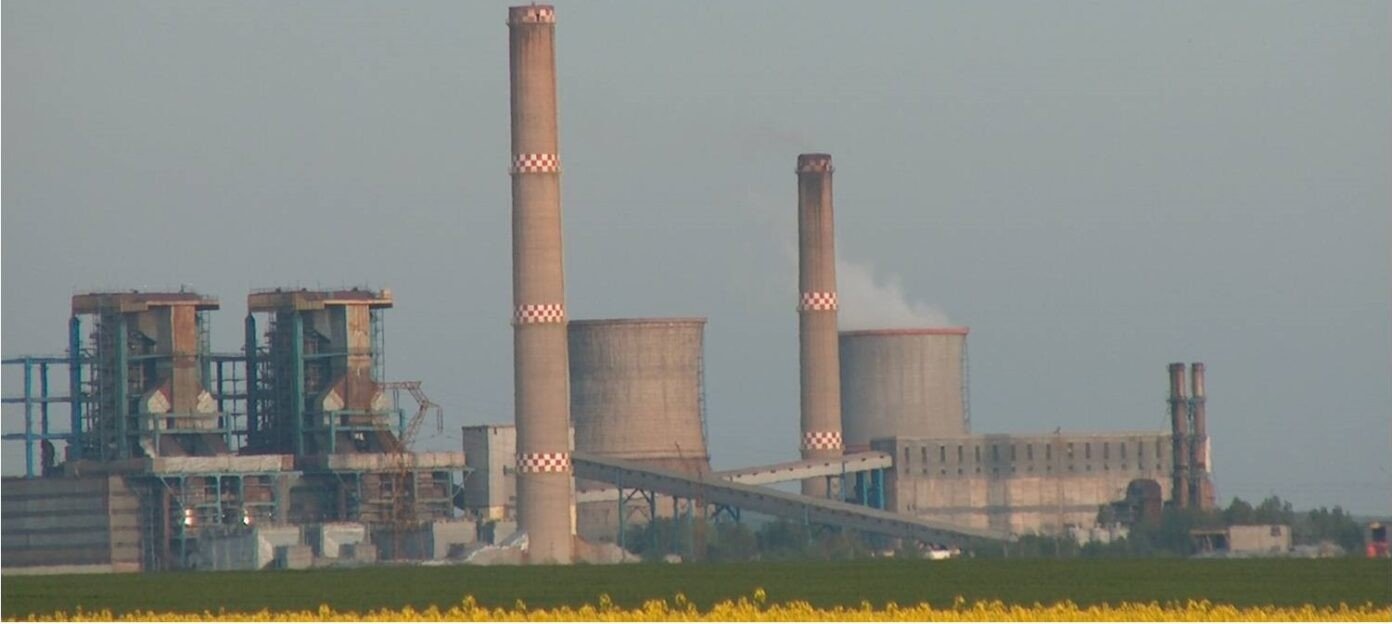 Панорама теплоэлектростанции «Электрочентрале Крайова» с дымовыми трубами и градирнями на фоне рапсового поля