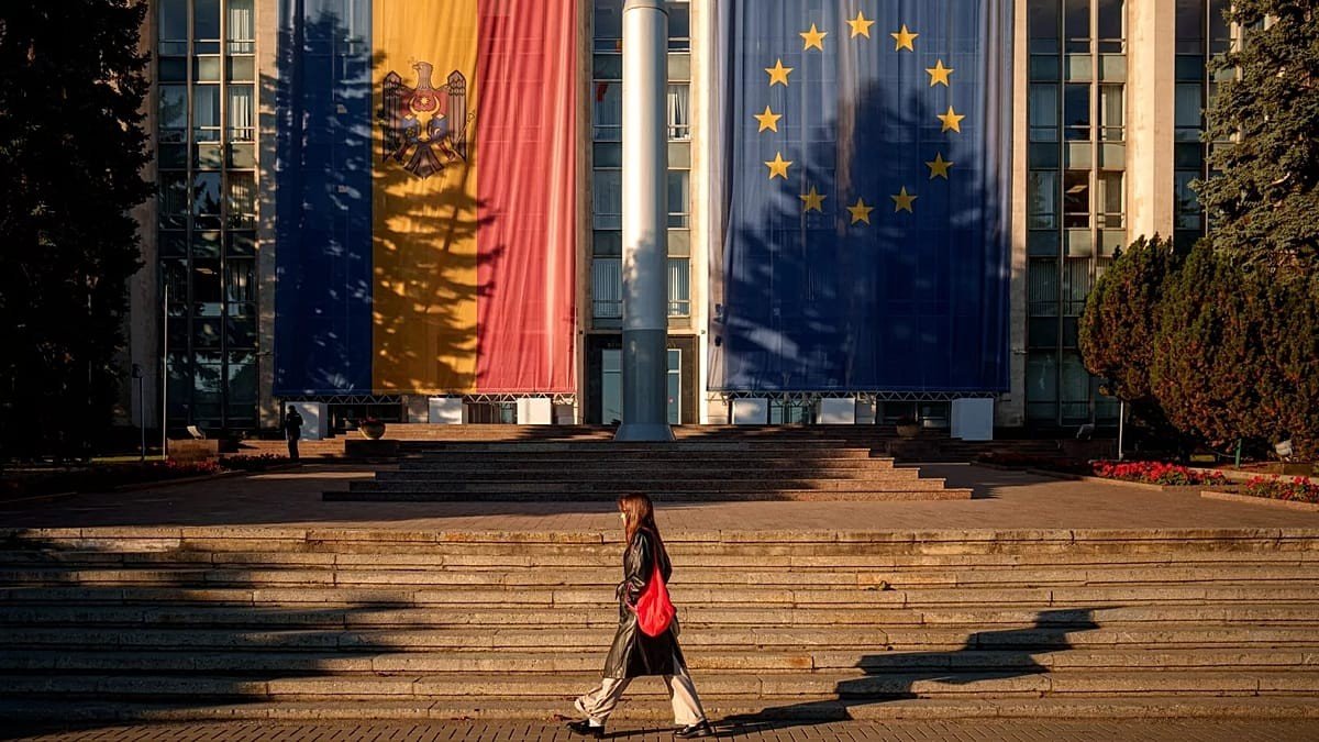 Moldova government building with giant Moldovan flag and EU flag, woman walking on steps. Фото: Euronews