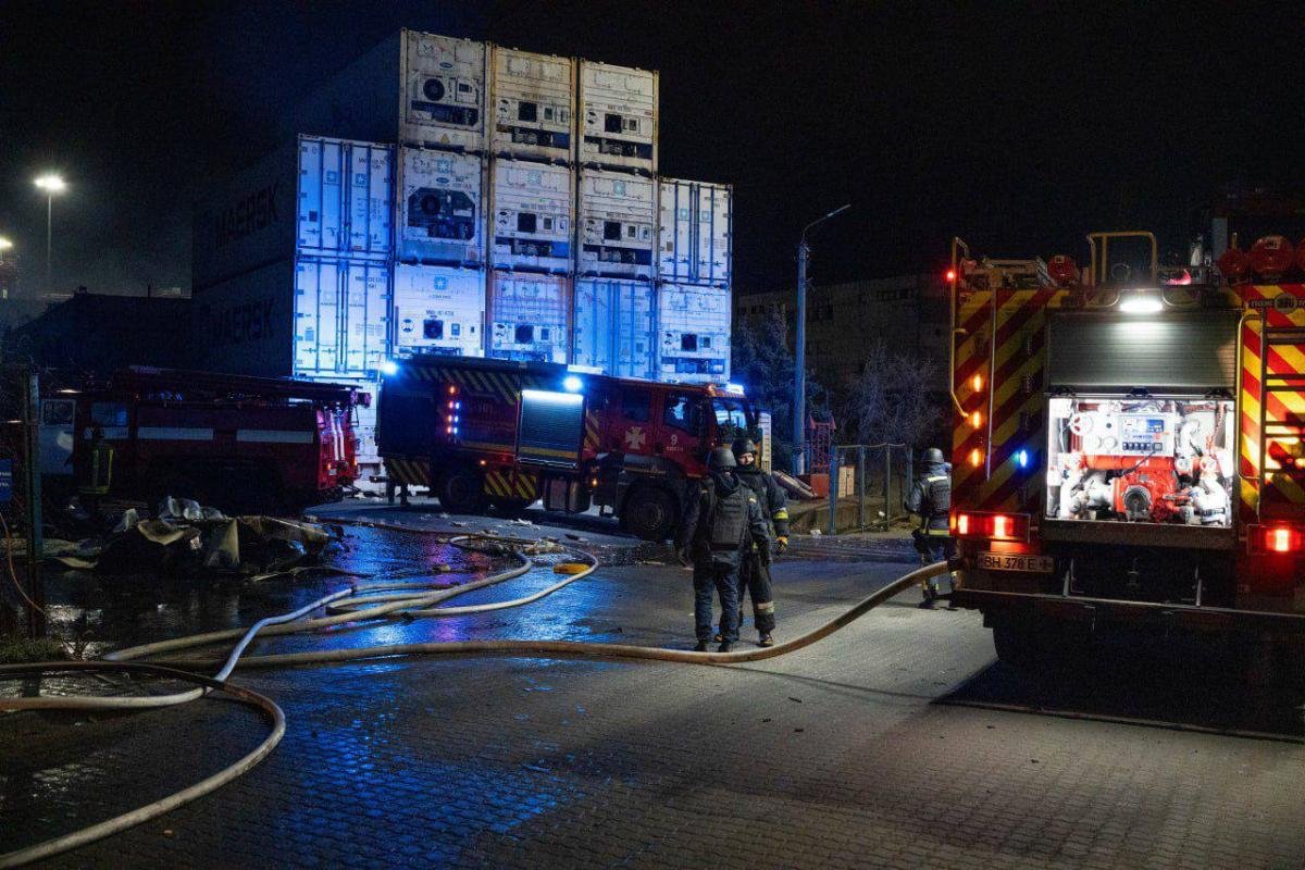 Night scene with fire trucks and emergency responders at container yard, blue emergency lights