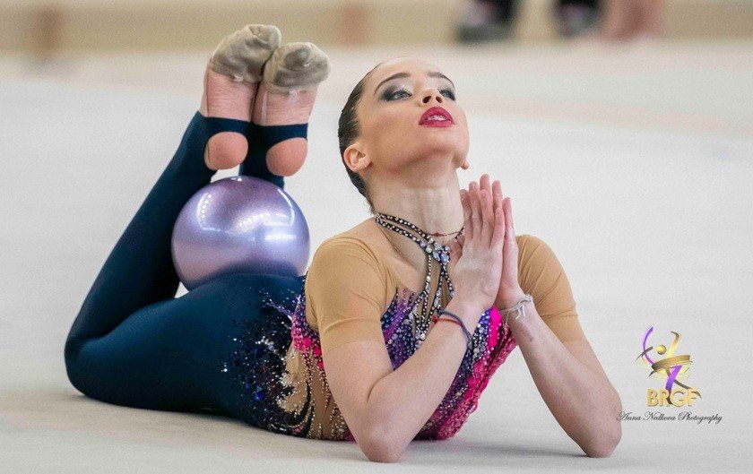 Болгарская гимнастка в художественной позе с мячом на гимнастическом ковре во время турнира в Любляне