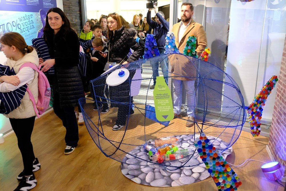 Посетители интерактивной выставки о пластике в Пуле рассматривают арт-инсталляцию в виде проволочной рыбы, наполненной пластиковыми крышками