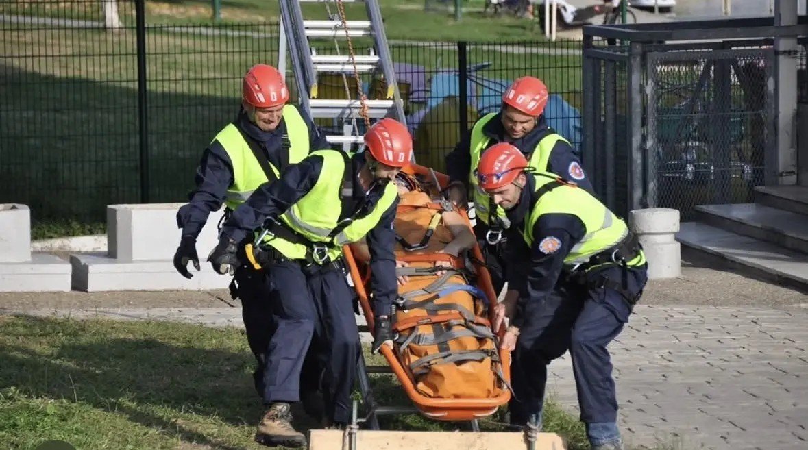 Учебные спасательные учения: четыре спасателя в желтых жилетах и оранжевых касках несут пострадавшего на носилках. Фото: Glas Šumadije