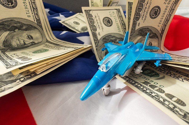 Игрушечный истребитель на фоне долларовых купюр и американского флага — иллюстрация к теме финансирования военного присутствия