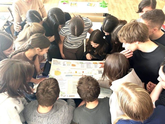 Школьники изучают информационный плакат о противодействии буллингу, собравшись вокруг материала в классе