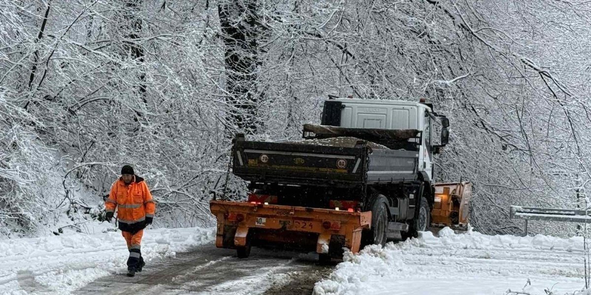 Рабочий дорожной службы в оранжевом жилете рядом со снегоуборочной техникой на заснеженной дороге