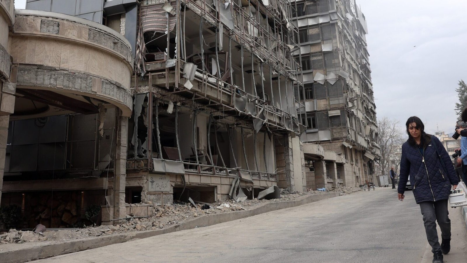Damaged building in Middle East conflict zone - woman walking past rubble. Фото: Balkan Insight (BIRN)