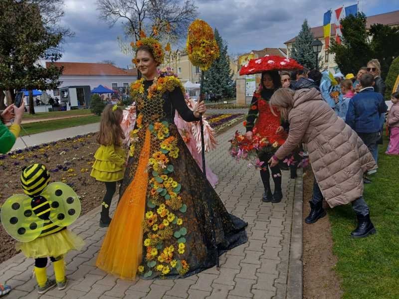 Женщина в платье с узором медовых сот и цветами идёт по аллее рядом с ребёнком в жёлто-чёрном костюме пчёлки