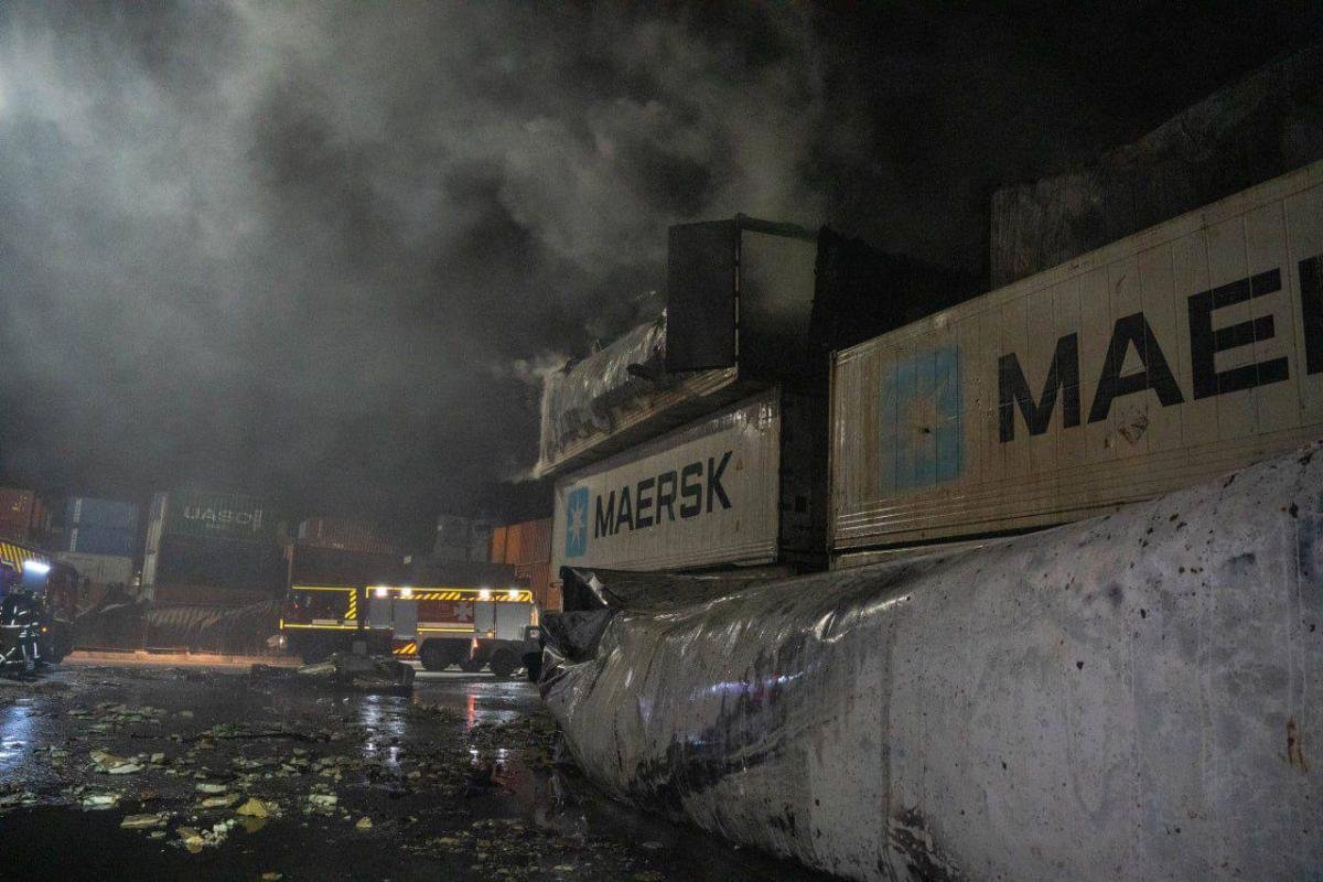 Port infrastructure damage with Maersk shipping containers, smoke rising, debris on ground