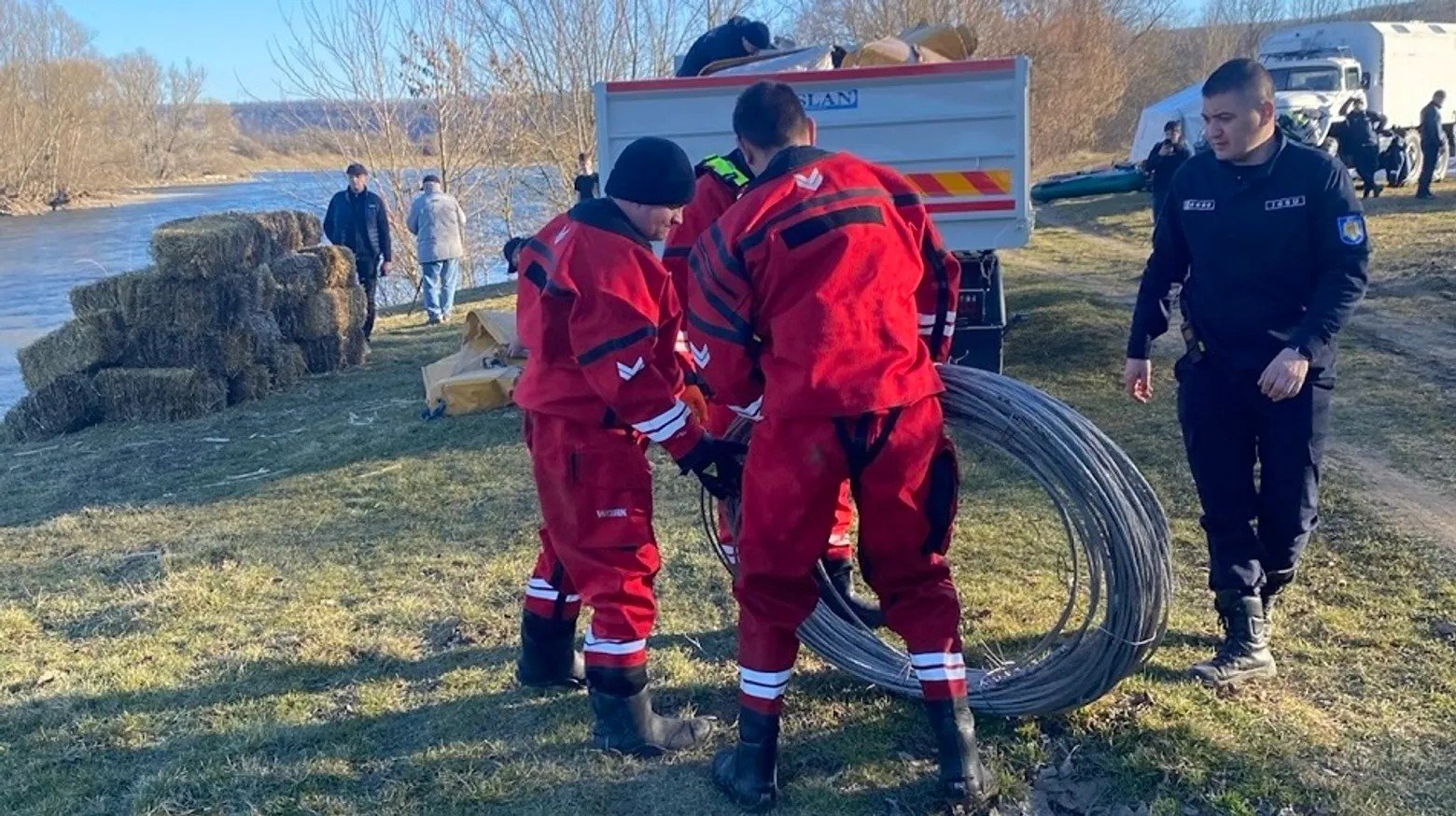 Спасатели в защитных костюмах разворачивают оборудование на берегу Днестра — рядом тюки сена для сбора нефтепродуктов