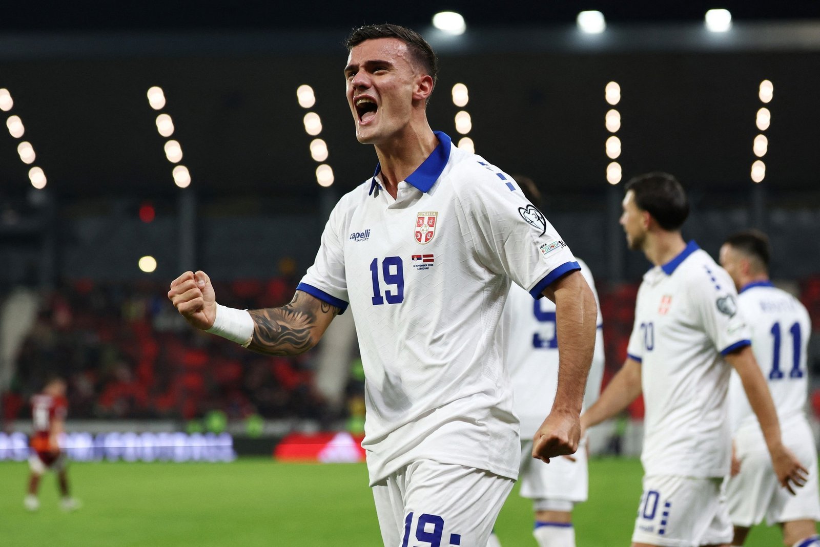Сербский футболист в белой форме с номером 19 эмоционально празднует забитый гол