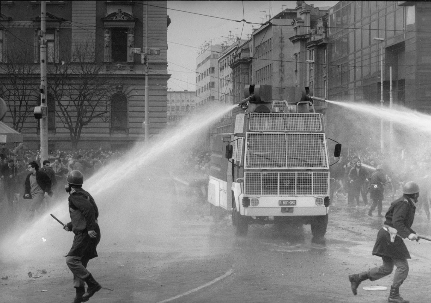 Полицейские в касках с дубинками бегут рядом с водомётом по улицам Белграда 9 марта 1991 года