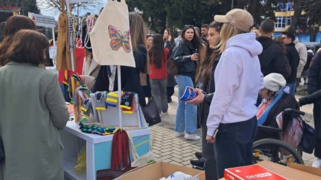 Уличная ярмарка с прилавком изделий ручной работы, посетители рассматривают сумки и украшения