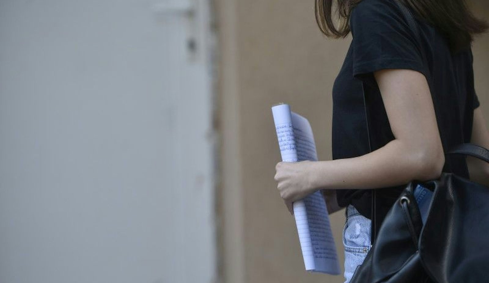 Ученица с тетрадями и рюкзаком выходит из школы после занятий