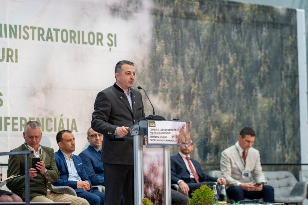 Спикер выступает с трибуны на фоне баннера с изображением лесов Румынии