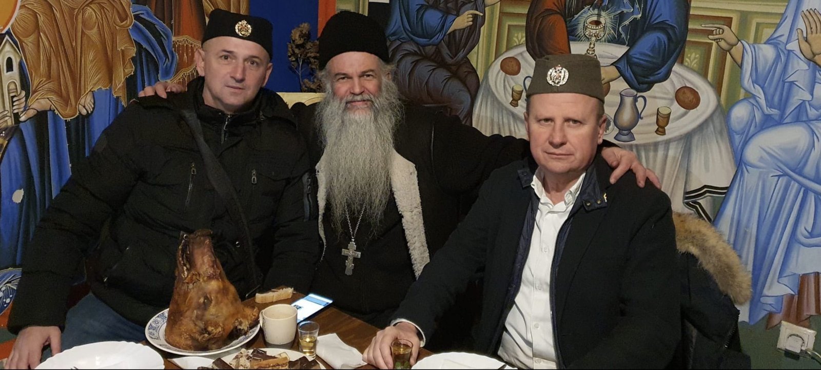 Три человека в четницких шапках встречаются с православным священником за столом. Фото: Istraga.ba