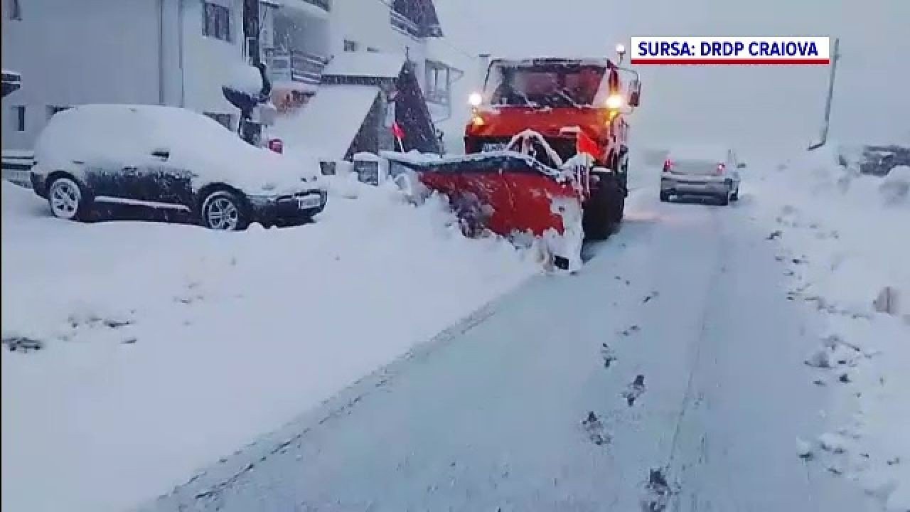 Снегоуборочная машина расчищает заснеженную улицу с припаркованными автомобилями