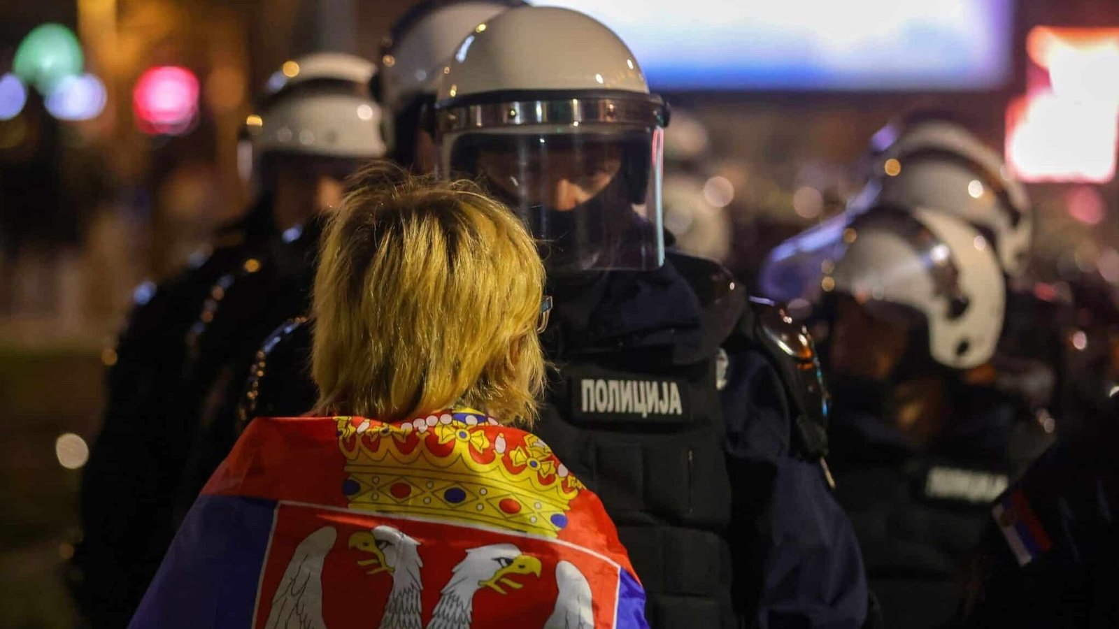 Участница протеста с сербским флагом стоит перед полицейским оцеплением в Белграде