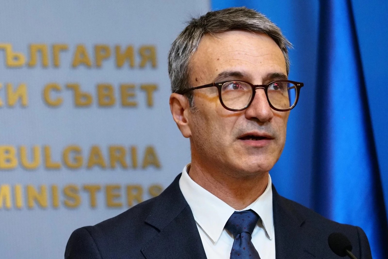 Правительственный чиновник на пресс-конференции в Министерском совете Болгарии на фоне надписи «България — Министерски съвет»
