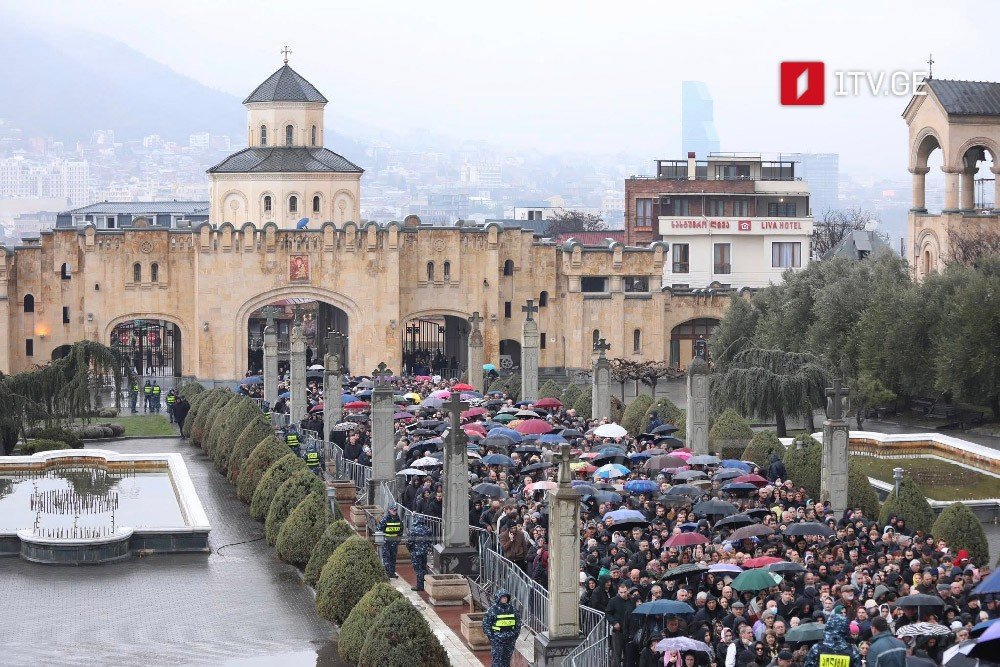 Тысячи людей с зонтами под дождём стоят в очереди к Собору Святой Троицы в Тбилиси, чтобы проститься с Патриархом Илией II