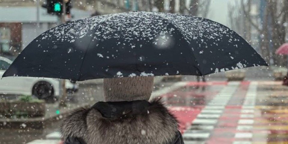 Пешеход с зонтом идёт по городской улице во время сильного снегопада