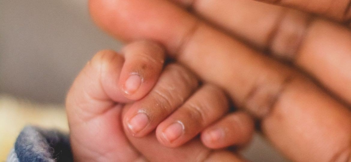 Маленькая ручка новорождённого держит палец взрослого