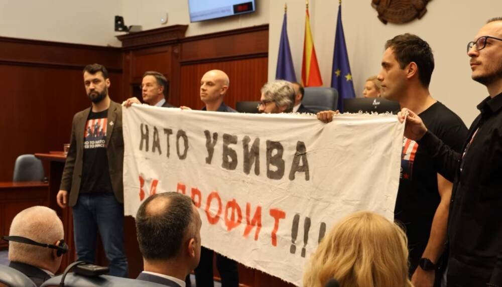 Депутаты партии «Левица» с транспарантом «НАТО УБИВА ЗА ПРОФИТ!!!» в Собрании Северной Македонии во время визита генерального секретаря НАТО