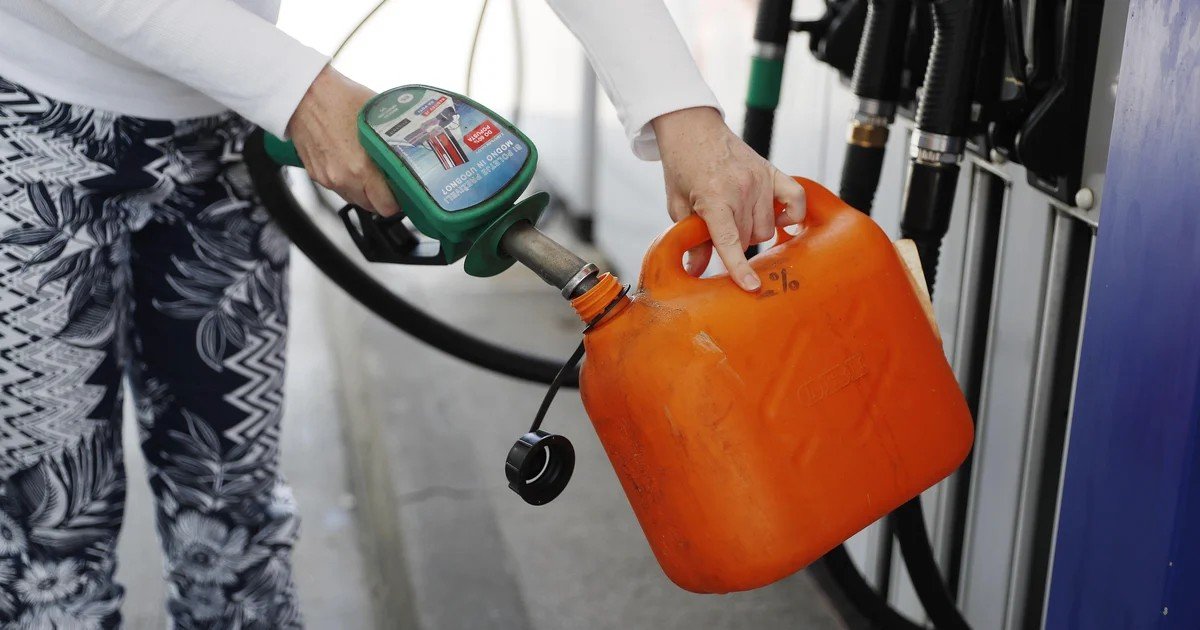 Человек наполняет оранжевую канистру бензином на заправочной станции