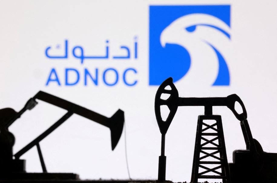 Логотип ADNOC на фоне силуэтов нефтяных качалок