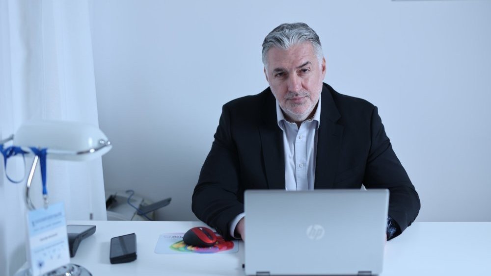 Man with grey hair at laptop in office setting. Фото: Danas