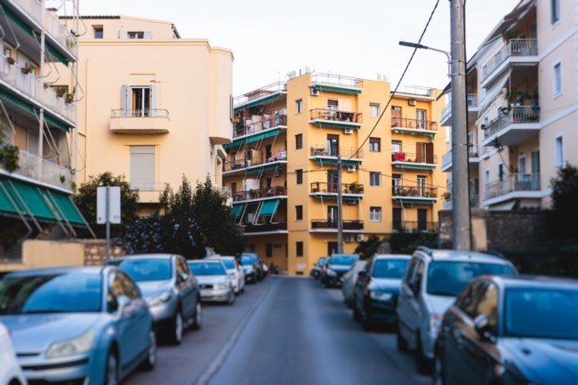 Жилая улица в центре Афин с многоэтажными домами, балконами и припаркованными автомобилями вдоль дороги