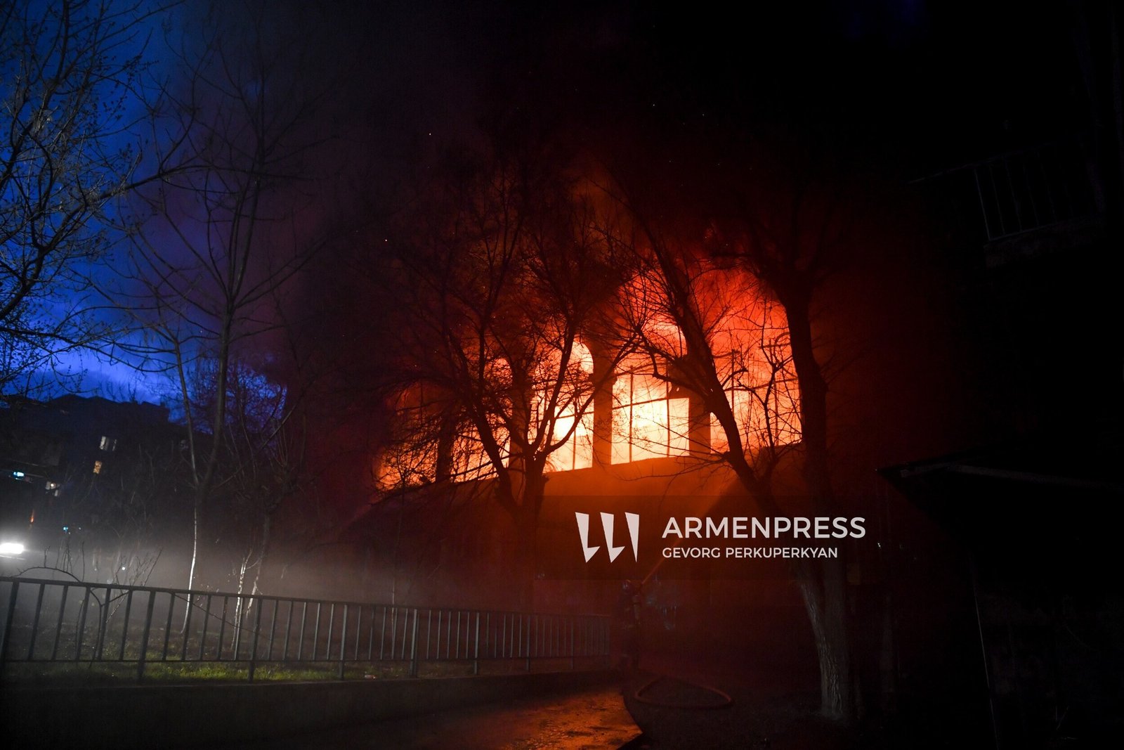 Общий вид пожара в Доме культуры «Каназ» ночью: пламя освещает здание сквозь голые деревья