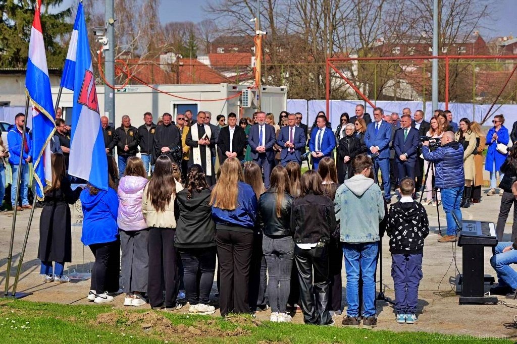 Школьники с флагами перед трибуной с официальными лицами на церемонии закладки камня нового спортзала в Слатине