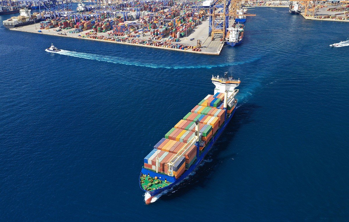 Контейнеровоз с разноцветными контейнерами отходит от оживлённого торгового порта, вид сверху