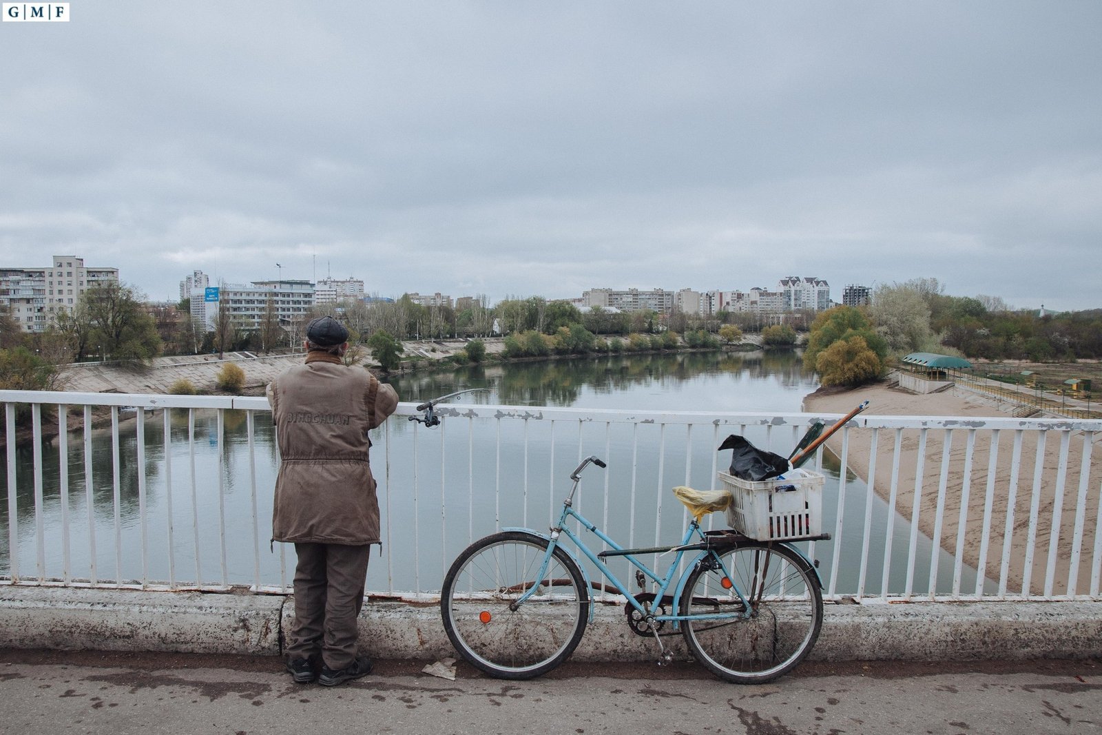 Мужчина ловит рыбу с моста через Днестр на фоне жилых кварталов Тирасполя