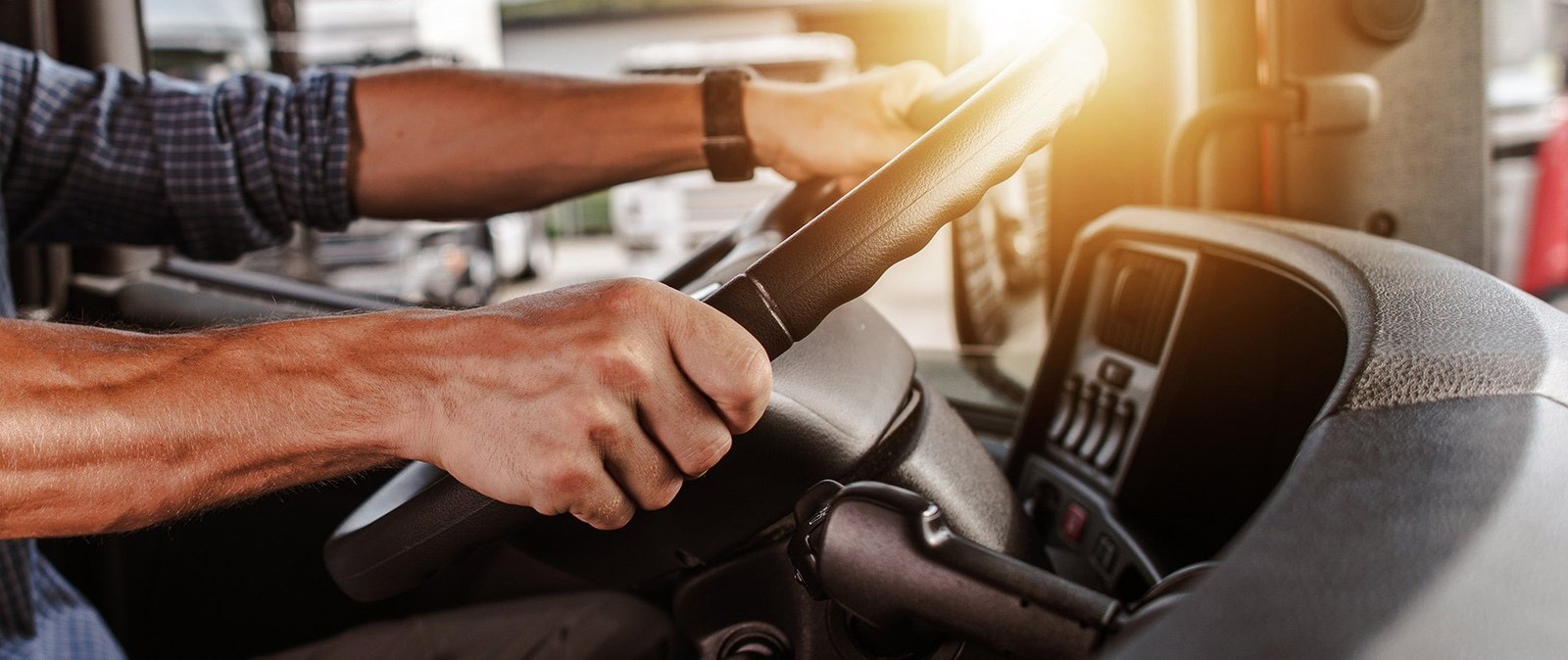 Руки водителя грузовика на рулевом колесе в кабине, освещённой солнечным светом