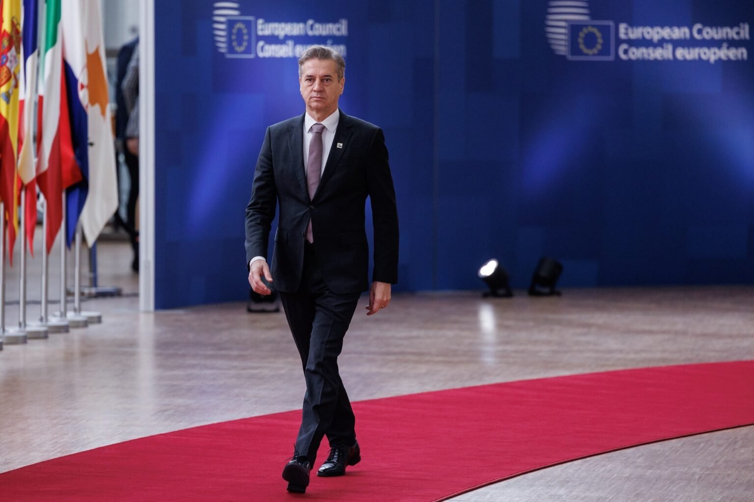 Премьер-министр Словении Роберт Голоб прибывает на саммит Европейского совета в Брюсселе, проходя по красной дорожке на фоне флагов стран ЕС